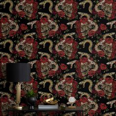 a desk with a lamp, skull and roses wallpaper on the wall next to it