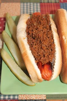 two hotdogs with chili and pickles on a green plate next to each other