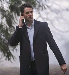 a man in a suit talking on a cell phone while walking through the foggy woods