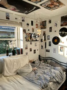 an unmade bed in a small room with pictures on the wall and ceiling above it