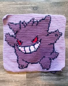 a pink and purple knitted pouch with an image of a smiling cat on it