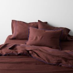 an unmade bed with brown sheets and blue piping on the pillowcases