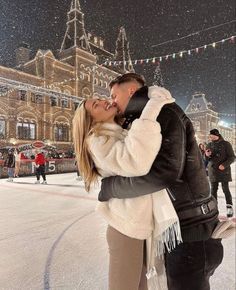 a man and woman kissing in front of an ice rink at night with christmas lights