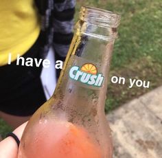 a person holding up a glass bottle with crush on it in front of some grass