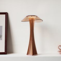 a table lamp sitting on top of a white shelf next to a framed photograph and coffee cup