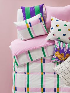 a bed with pink, green and white sheets and pillows next to a pillow case