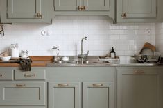 a kitchen with green cabinets and white tile backsplashing, gold handles on the faucets