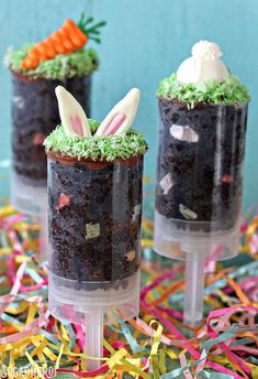 chocolate cupcakes decorated with bunny ears and carrots in plastic cups on top of confetti streamers