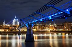 a bridge that is over some water with buildings in the background and lights on it