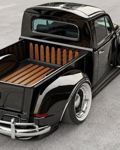 an old black pickup truck parked in a parking lot with its bed up to the ground