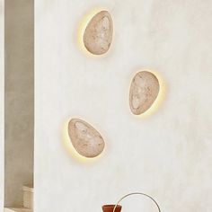 three stone lights are on the wall above a table with a vase and potted plant