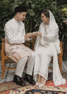 a man and woman sitting on top of a wooden bench in front of a bush