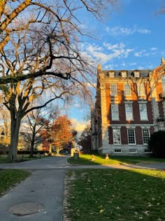 an old brick building with trees in the foreground and green grass on either side