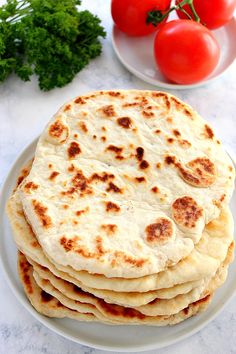 a stack of flat bread on a plate next to tomatoes