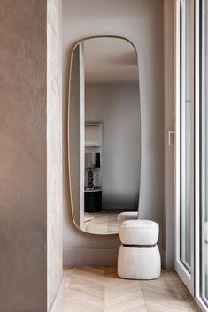 a large mirror sitting on top of a wooden floor next to a white stool in front of a window