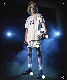 a soccer player is holding a ball in his hands and posing for the camera with blue lights behind him