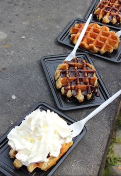 three waffles with whipped cream and chocolate syrup on them sitting on black trays