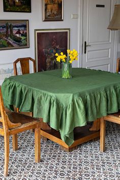 a green table cloth with yellow flowers in a vase on top and chairs around it