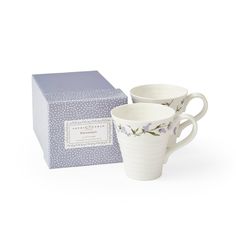 two white coffee cups sitting next to a box