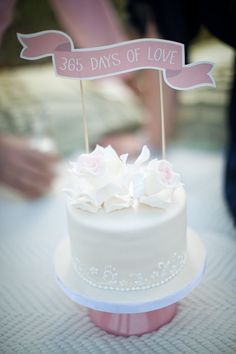 a white cake sitting on top of a table covered in frosting and pink ribbon