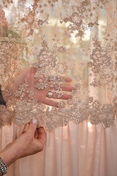 a person is holding something in front of a window that has lace on it and flowers all over it