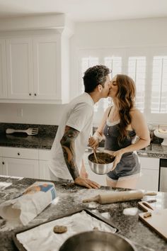 a man and woman are kissing in the kitchen while they prepare food for their dinner