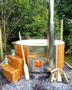 an outdoor hot tub surrounded by logs and firewood with a wood burning stove in the middle