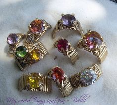 six different colored stones in gold tone setting on white cloth with words written below them