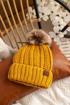 a yellow knitted hat sitting on top of a brown pillow next to a white flower