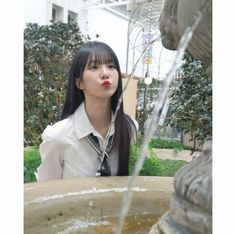 a woman sitting in front of a fountain with water pouring out of it's mouth