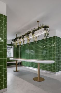 an empty room with green tiled walls and plants hanging from the ceiling over the table