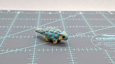 a blue and yellow frog figurine sitting on top of a cutting board next to a ruler