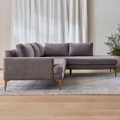 a gray couch sitting on top of a wooden floor next to a white curtained window