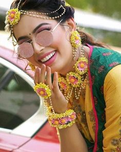 a woman in yellow and green outfit with flowers on her head posing next to a red car