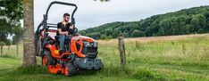 a man riding on the back of an orange lawn mower next to a tree