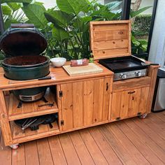 an outdoor bbq grill on top of a wooden table next to a potted plant