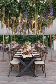 an outdoor dining area with tables and chairs covered in flowers, greenery and hanging lights