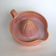 an orange and pink ceramic dish on a white surface with a small plant in the center