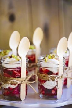 mason jars filled with strawberries and topped with wooden spoons on top of a table