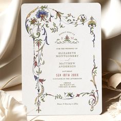 a wedding card with an ornate design on the front and back, sitting next to some flowers