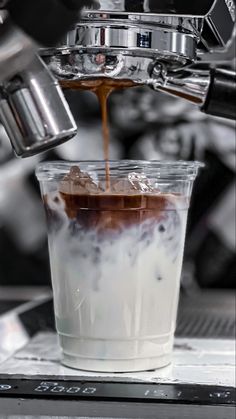 coffee being poured into a cup with ice and liquid in it on top of a machine