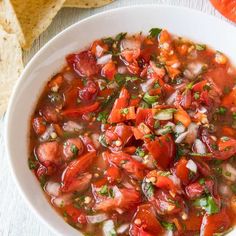 a white bowl filled with vegetable soup next to tortilla chips on a table