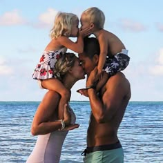 a group of people standing on top of a beach next to the ocean with their arms around each other