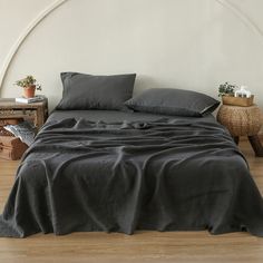 a bed with black sheets and pillows in a white room next to a wooden table