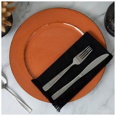 an orange plate topped with a fork and knife next to a black napkin on top of it