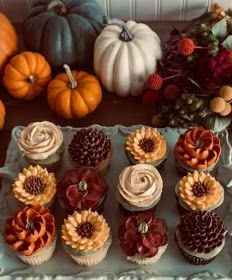 there are many cupcakes on the tray with flowers and pumpkins in the background