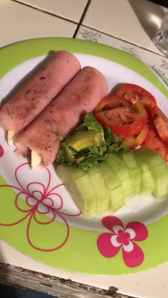 two sausages, tomatoes and cucumber are on a green and white plate