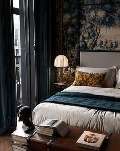 a large bed sitting next to a window in a room with blue curtains and a painting on the wall