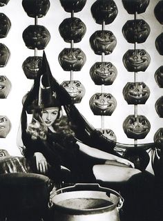 a black and white photo of a woman sitting in front of pumpkins hanging from the ceiling