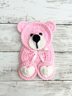 a pink crocheted teddy bear hanging on a white wooden wall